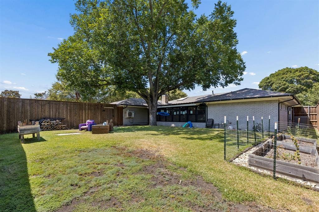 2408 Grandview Drive, Plano, TX 75075 Expansive backyard featuring a mature tree, wood privacy fencing, light-colored brick exterior, and raised garden beds