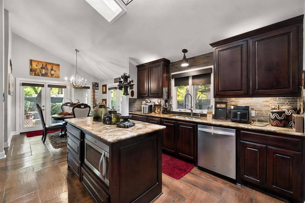 656 The Meadows Parkway, DeSoto, TX 75115 Kitchen featuring dark wood cabinetry, a central island with a built-in microwave, stainless steel appliances, and a skylight