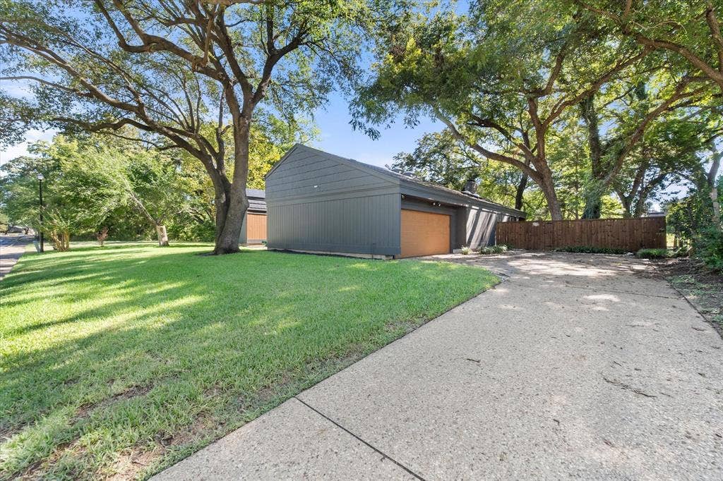 656 The Meadows Parkway, DeSoto, TX 75115 Sloped roofline exterior with dark siding, wood-finish garage door, concrete driveway, and mature landscaping