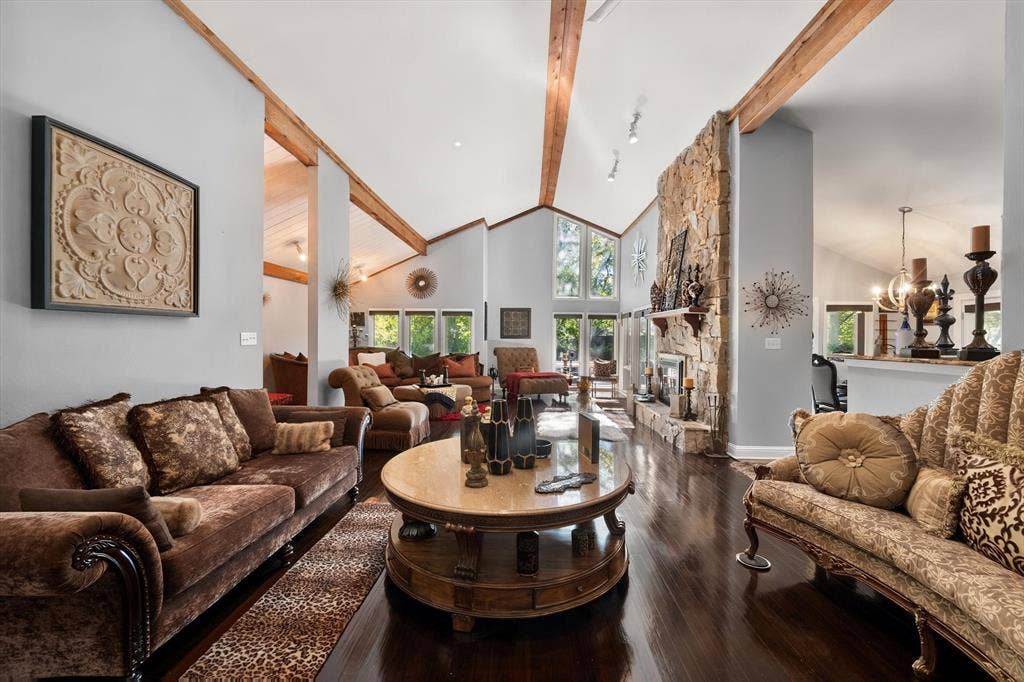 656 The Meadows Parkway, DeSoto, TX 75115 Vaulted ceilings with exposed wood beams, a stone-clad fireplace, dark wood-finish flooring, and large picture windows