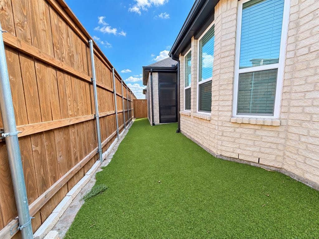 1613 Sandhill Lane, Celina, TX 75009 Fenced exterior corridor featuring artificial turf, light brick facade, and multiple windows with blinds