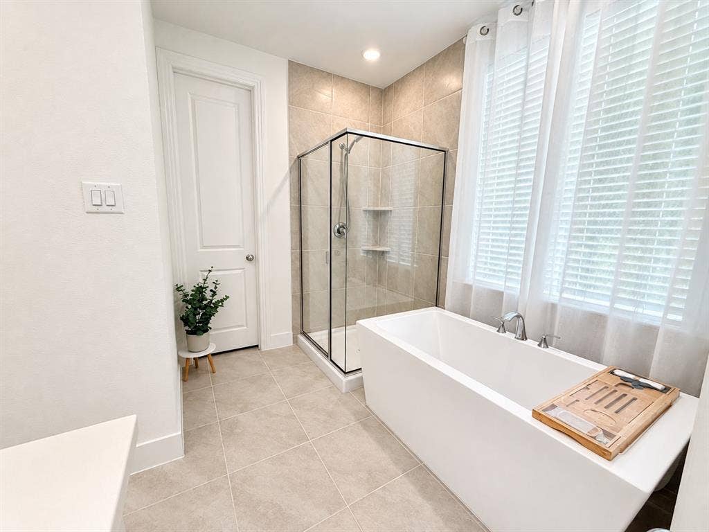 1613 Sandhill Lane, Celina, TX 75009 Freestanding soaking tub with chrome fixtures, tiled walk-in shower with glass enclosure, large windows with white blinds, and light-toned floor tile