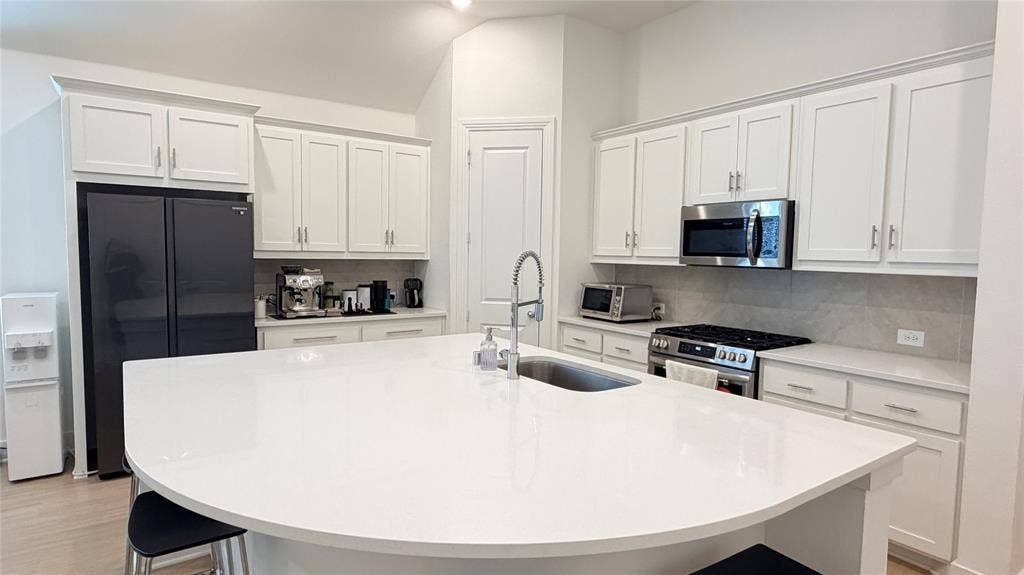 1613 Sandhill Lane, Celina, TX 75009 Expansive kitchen island with a curved countertop, stainless steel appliances, white cabinetry with silver-tone hardware, and a tile backsplash