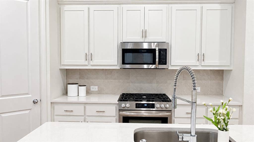 1613 Sandhill Lane, Celina, TX 75009 White shaker-style cabinetry, stainless steel appliances, light-toned backsplash, light-toned countertops, and a stainless steel sink with a high-arch faucet