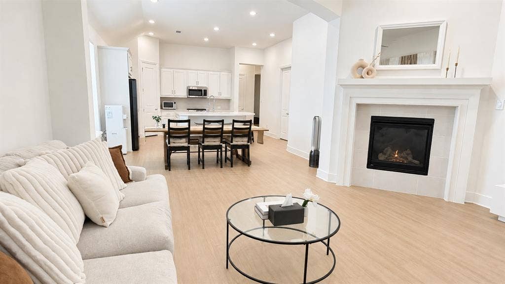 1613 Sandhill Lane, Celina, TX 75009 Open-concept living area featuring light wood-finish flooring, a built-in fireplace with a mantel, recessed lighting, and a kitchen with white cabinetry and stainless steel appliances