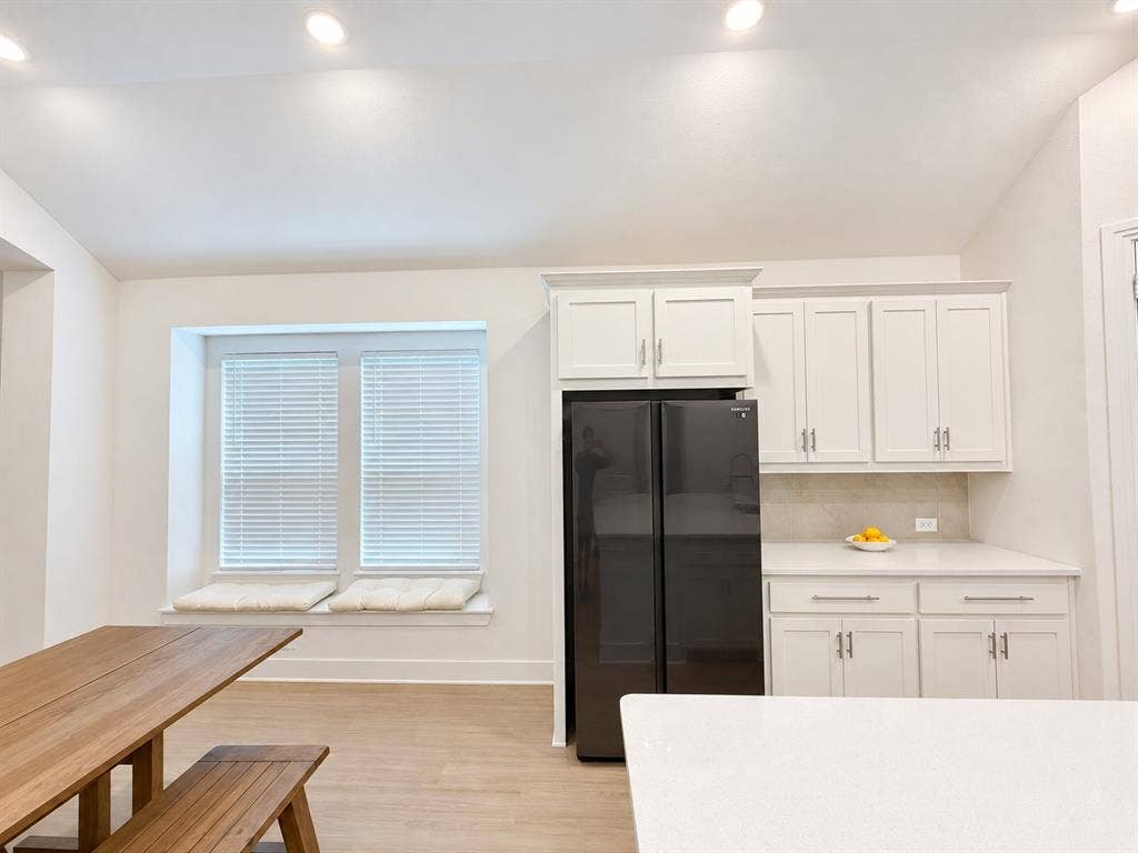 1613 Sandhill Lane, Celina, TX 75009 Recessed lighting, white shaker-style cabinetry, light-toned wood-finish flooring, built-in window seating, and a large black refrigerator