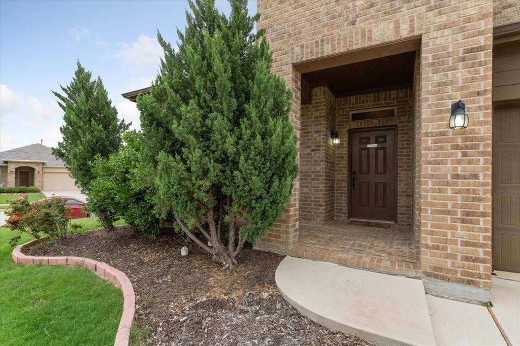 1713 Falling Star Drive, Fort Worth, TX 76052 Brick exterior with a covered entry, dark paneled door, and exterior lighting fixtures