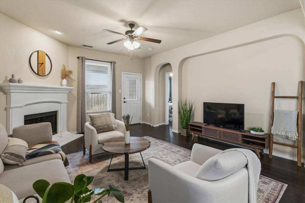 1713 Falling Star Drive, Fort Worth, TX 76052 Living area with rich wood-finish flooring, a white mantel fireplace, and a ceiling fan with integrated lighting