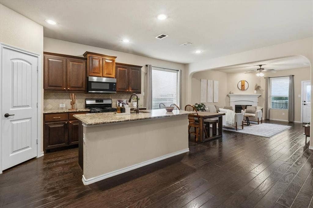 1713 Falling Star Drive, Fort Worth, TX 76052 Kitchen with wood-finish flooring, dark wood cabinetry, stainless steel appliances, and a granite-topped island with a breakfast bar