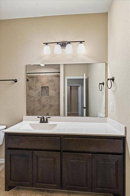 1713 Falling Star Drive, Fort Worth, TX 76052 White countertop with an integrated sink, dark wood-finish vanity, large wall-mounted mirror, and a four-light fixture