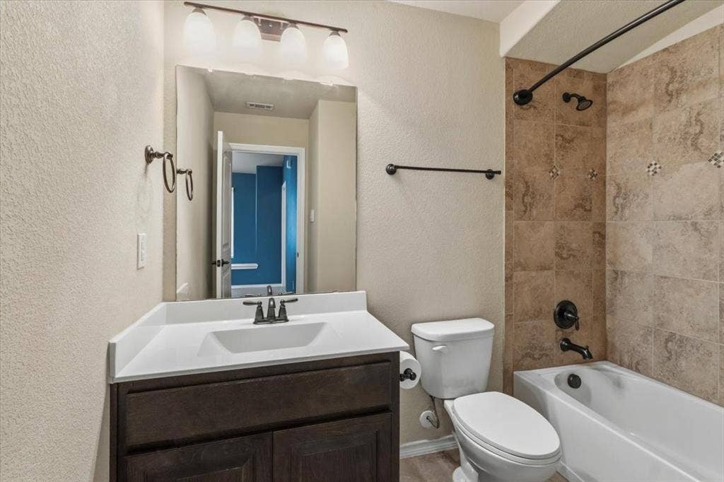 1713 Falling Star Drive, Fort Worth, TX 76052 Vanity with a single basin, tiled bath and shower combination, dark wood-finish cabinetry, and brushed bronze fixtures