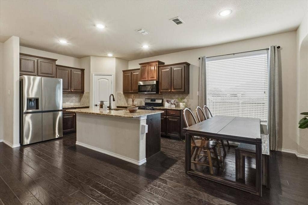 1713 Falling Star Drive, Fort Worth, TX 76052 Kitchen featuring wood-finish flooring, dark wood cabinetry, a center island with a light-toned countertop, and stainless steel appliances