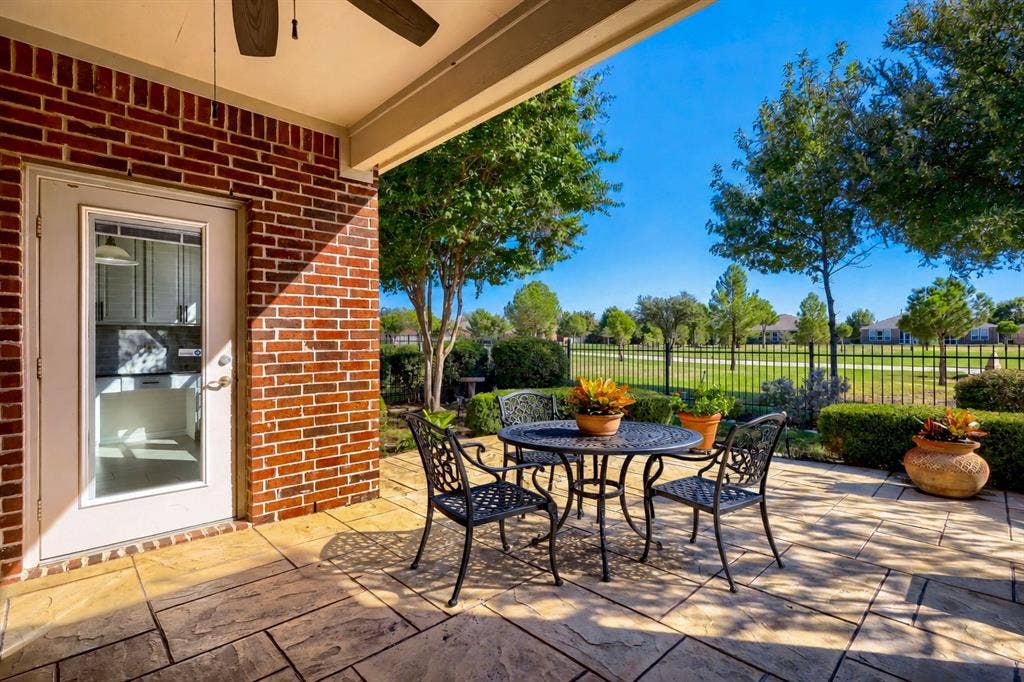 Covered patio with stamped concrete flooring, brick exterior, and a ceiling fan