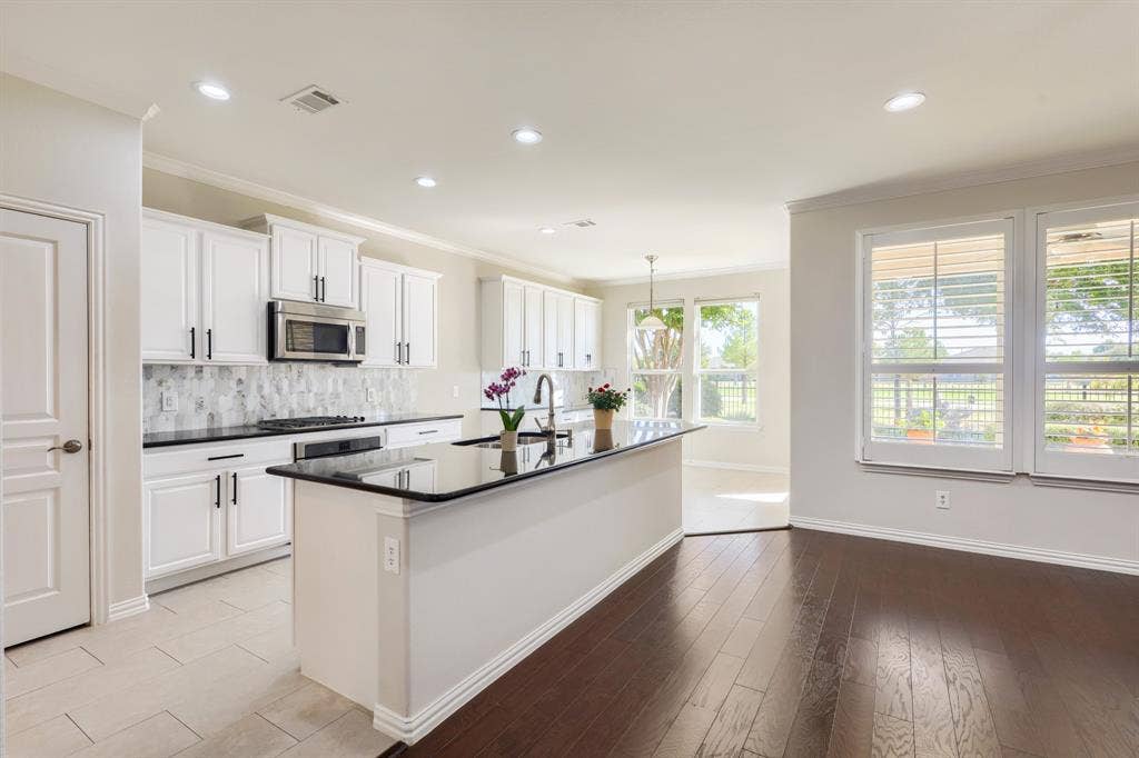 Kitchen featuring white cabinetry, a dark countertop island, stainless steel microwave, and tile backsplash