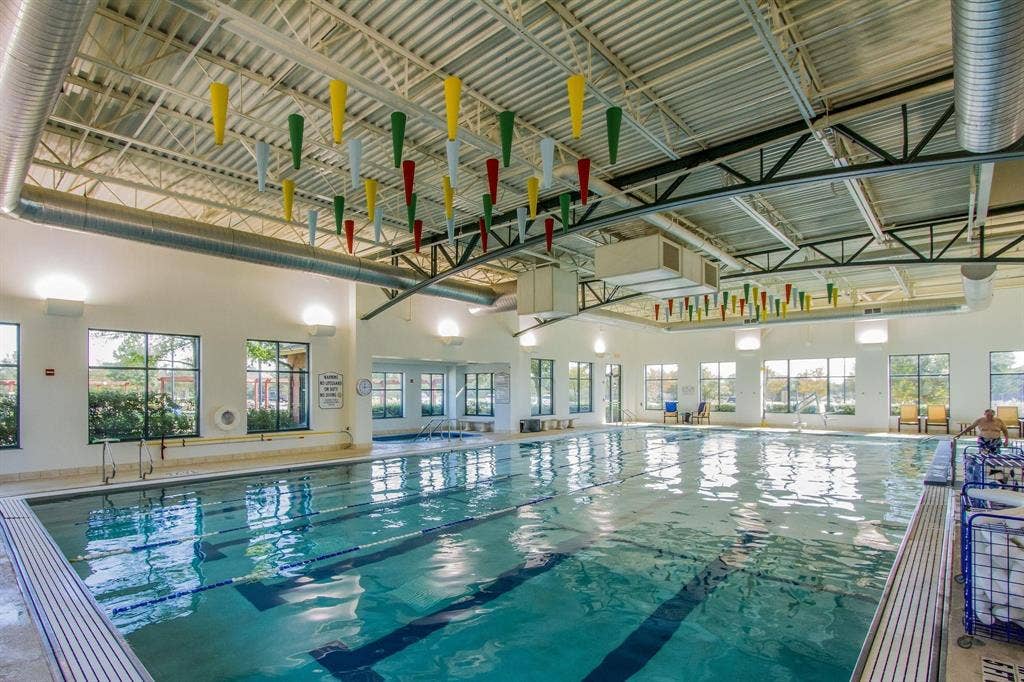 Indoor swimming pool with lane markers, light-colored pool deck, multiple windows, and exposed ceiling structure