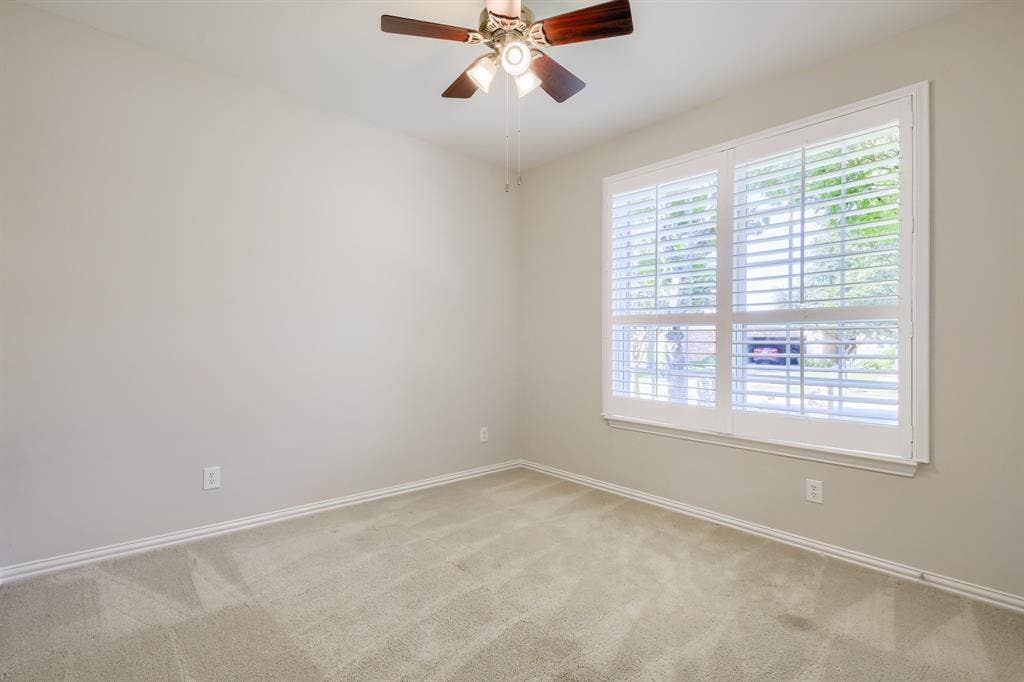 Warm neutral wall color, plush carpet flooring, white plantation shutters, and a ceiling fan with integrated lighting