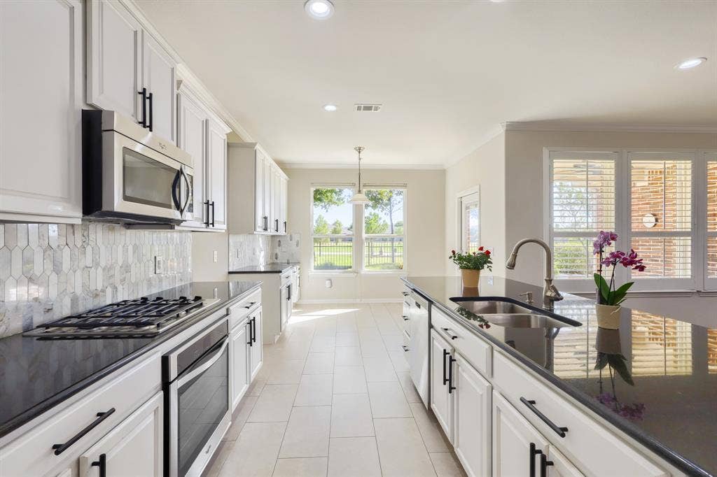 Kitchen featuring white shaker cabinetry, black countertops, stainless steel appliances, a tile backsplash, and light tile flooring