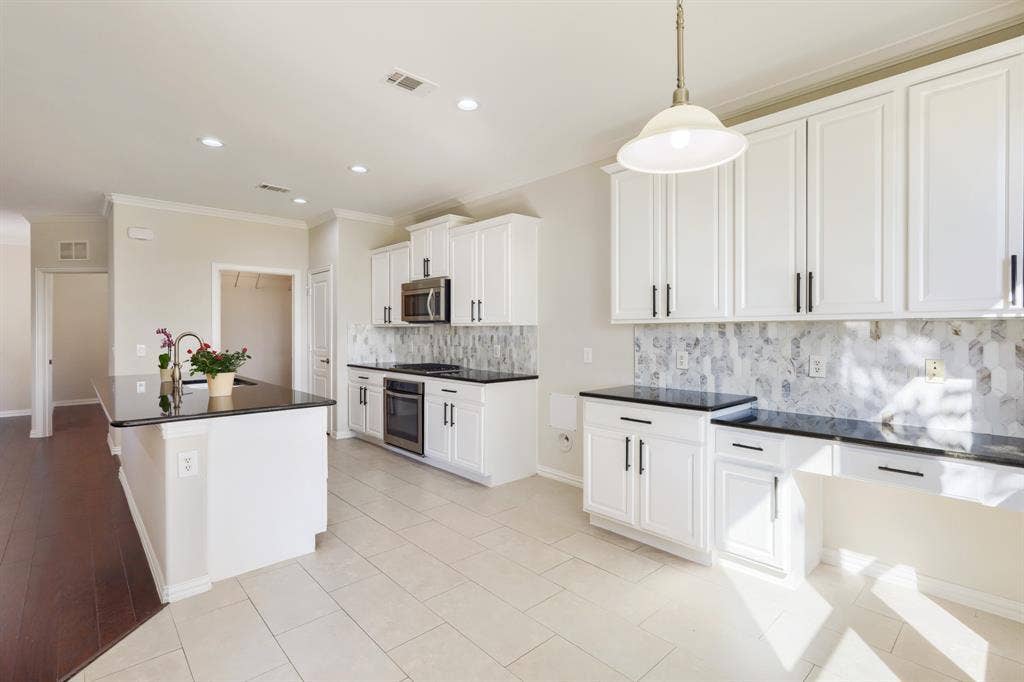 White cabinetry with black hardware, Quartz countertops, built-in stainless steel microwave, and tile flooring