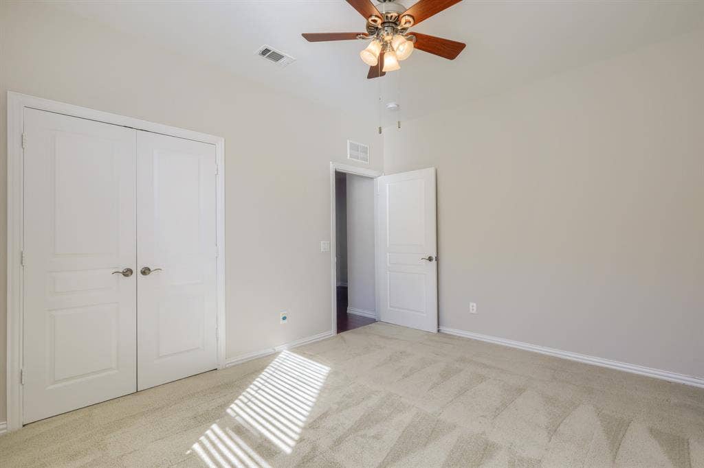 Plush carpet flooring, light neutral wall tones, and a ceiling fan with integrated lighting