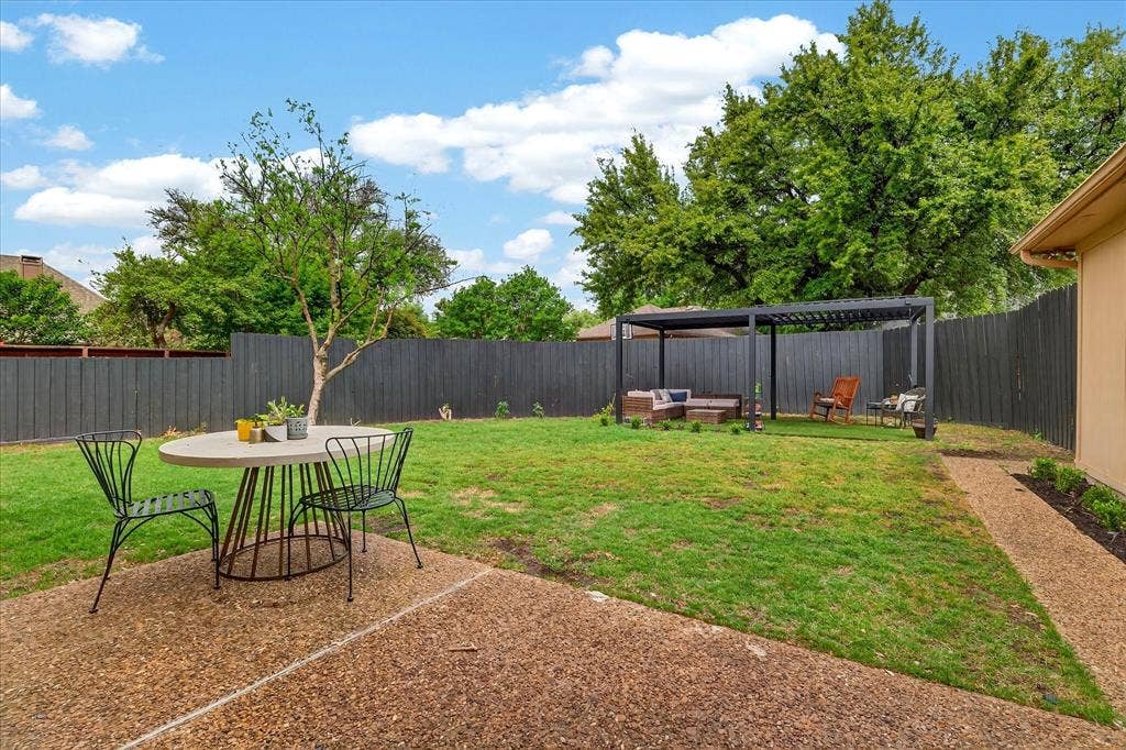 Expansive backyard featuring a pergola, gravel pathway, concrete patio, and dark-stained privacy fencing
