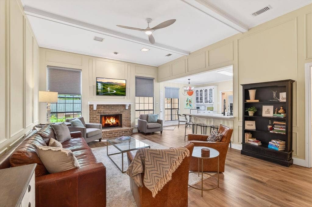 Living area featuring wood-finish flooring, a brick fireplace with a white mantel, and beamed ceilings