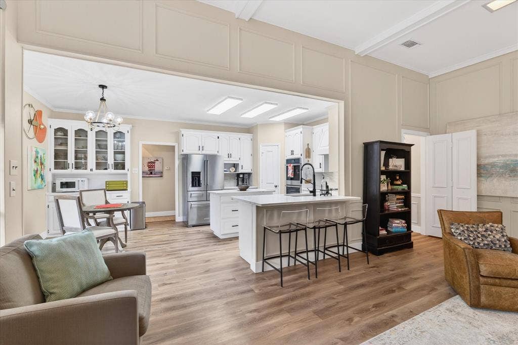 Open-concept living area with wood-finish flooring, a kitchen featuring white cabinetry, a central island with counter seating, stainless steel appliances, and recessed lighting