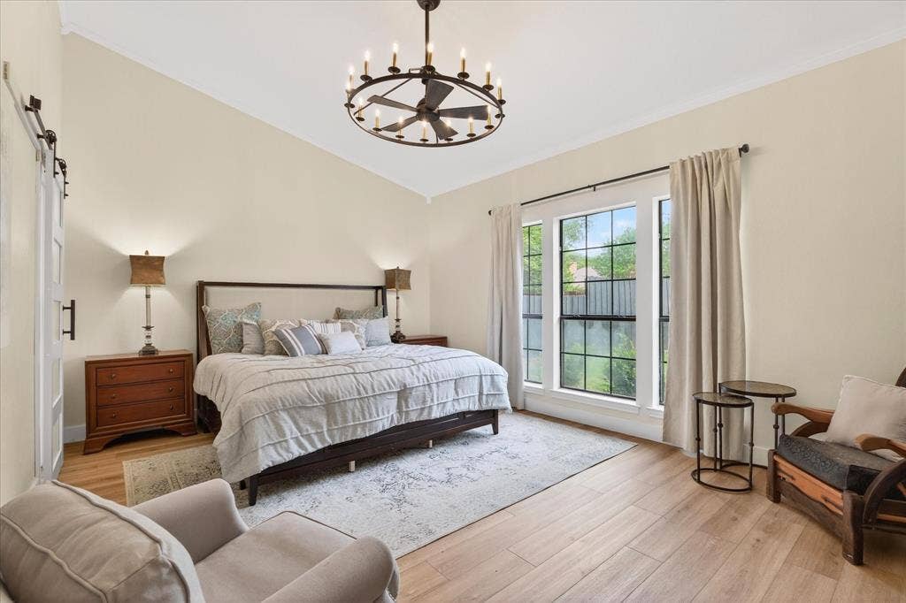 Vaulted ceiling with an iron chandelier, light wood-finish flooring, and a large window with black grilles
