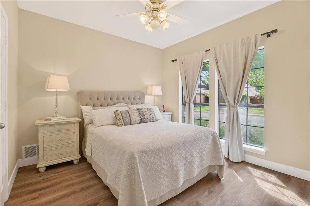Wood-finish flooring, tufted upholstered headboard, dual windows, and ceiling fan with integrated lighting