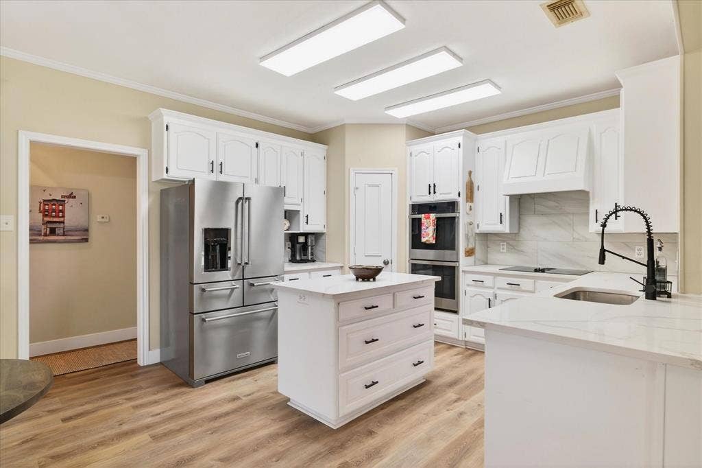 White cabinetry with dark hardware, wood-finish flooring, a central island, stainless steel appliances, and light-toned countertops