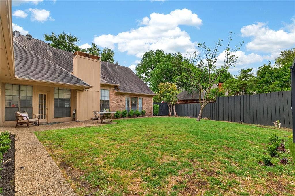 Expansive backyard with a manicured lawn, brick exterior, dedicated patio area, and a mature tree