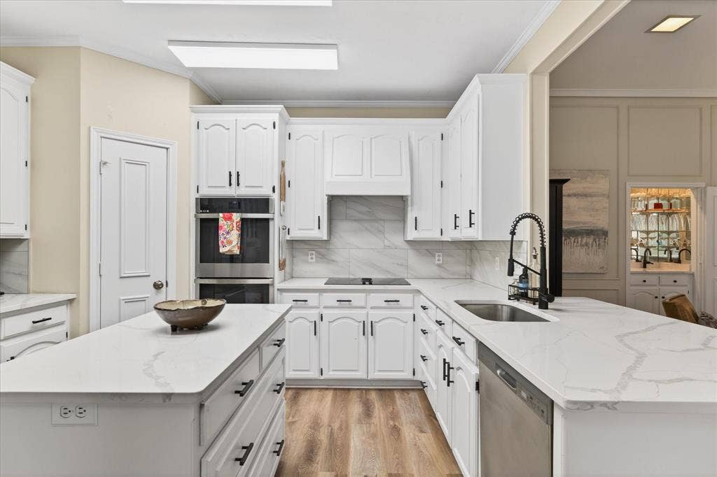 White cabinetry with black hardware, stainless steel appliances, wood-finish flooring, white countertops, and a white tile backsplash