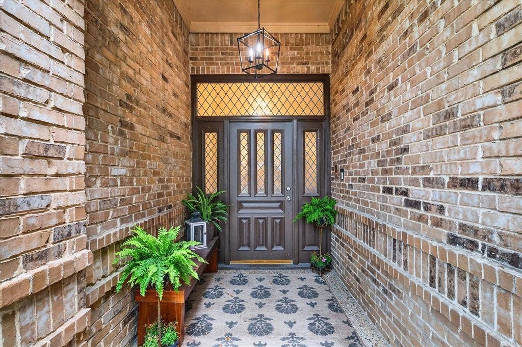Brick exterior facade featuring an ornate wood-paneled door with sidelights, a transom window with leaded glass, and an overhead lantern-style light fixture