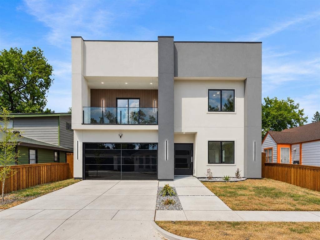 1711 Kraft Street, Dallas, TX 75212 Contemporary architecture featuring a two-tone facade, glass balcony railing, full-light garage door, concrete driveway, and integrated exterior lighting