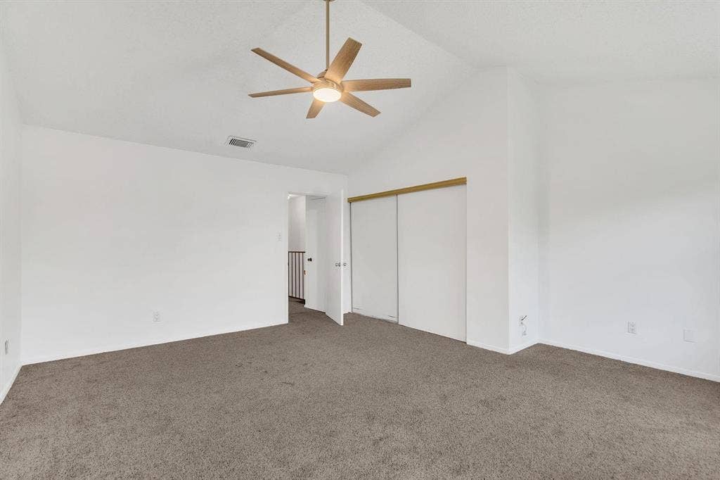 Vaulted ceiling, ceiling fan with integrated lighting, carpeted flooring, sliding closet doors, and neutral wall tones
