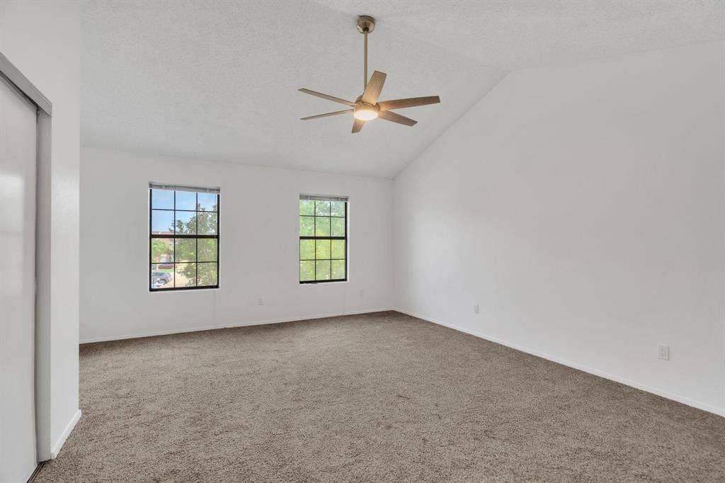 Vaulted ceiling with a ceiling fan and integrated lighting, two double-hung windows, wall-to-wall carpeting, and a built-in closet with sliding doors