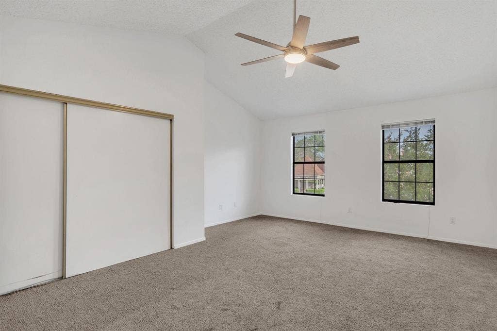 Vaulted ceiling with a ceiling fan, two windows, carpet flooring, and sliding closet doors