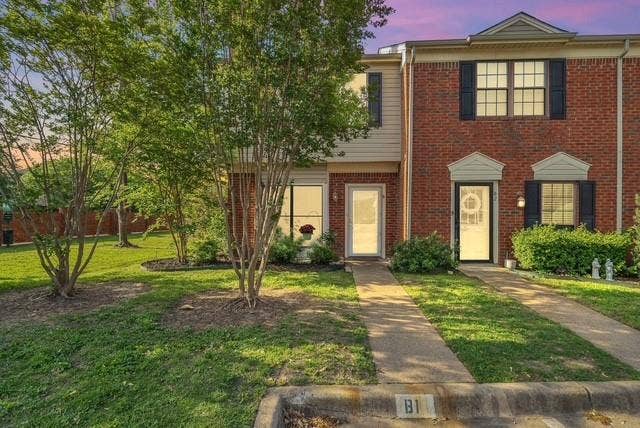 Brick facade with accent siding, individual entryways, mature trees, and a concrete paver walkway