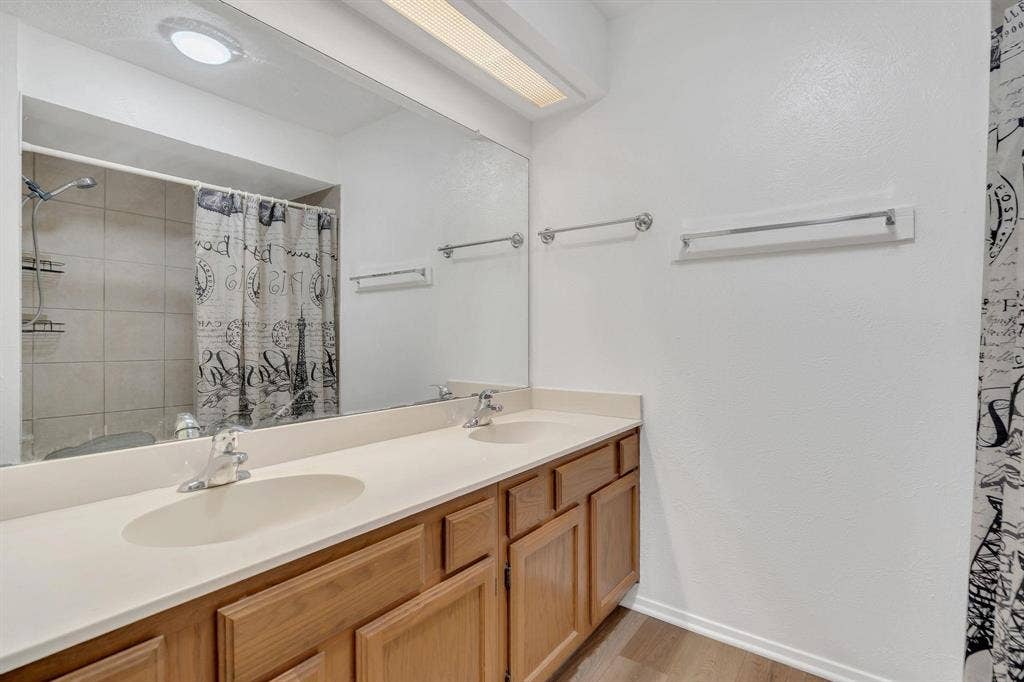 Double vanity with integrated sinks, wood-finish cabinetry, a full-width mirror, and a tiled shower-tub combination