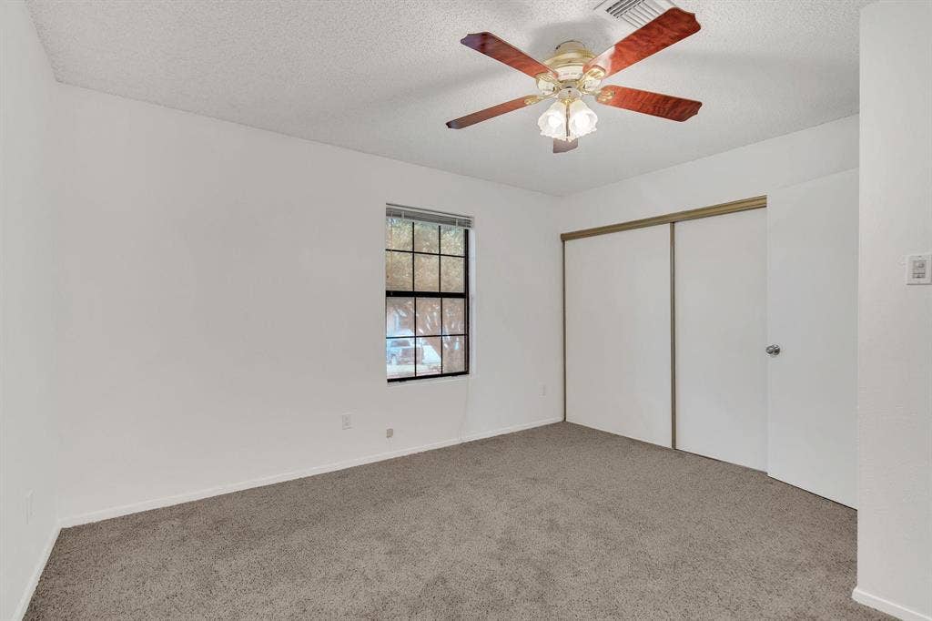 Room featuring a window, ceiling fan with light fixture, carpeted flooring, and sliding closet doors