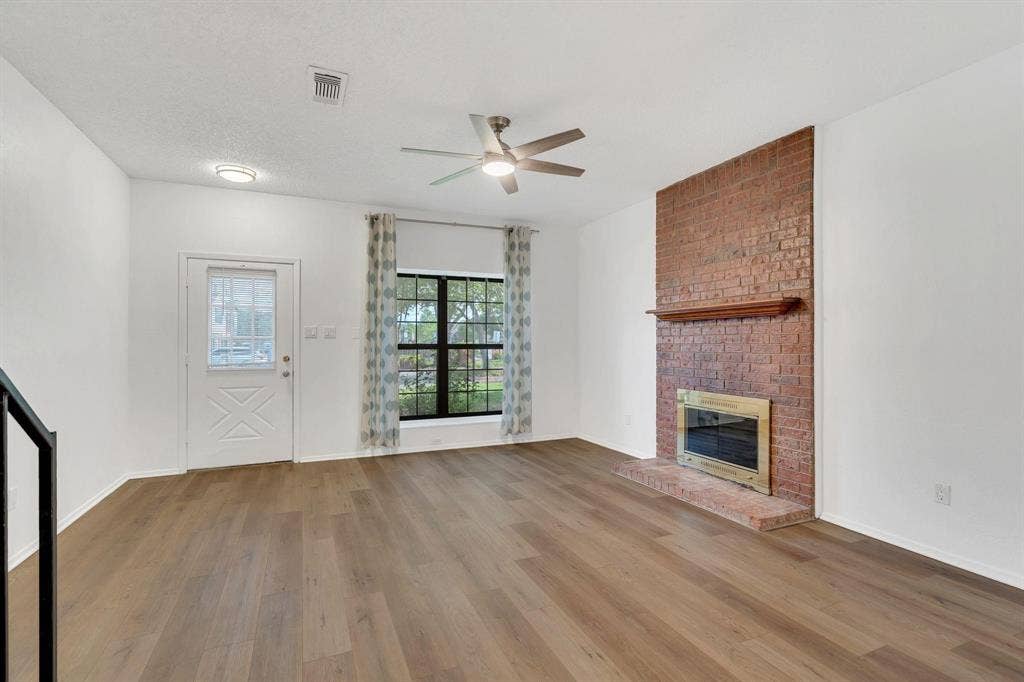 Wood-finish flooring throughout, brick fireplace with a wood mantel, ceiling fan, and a transom-style door