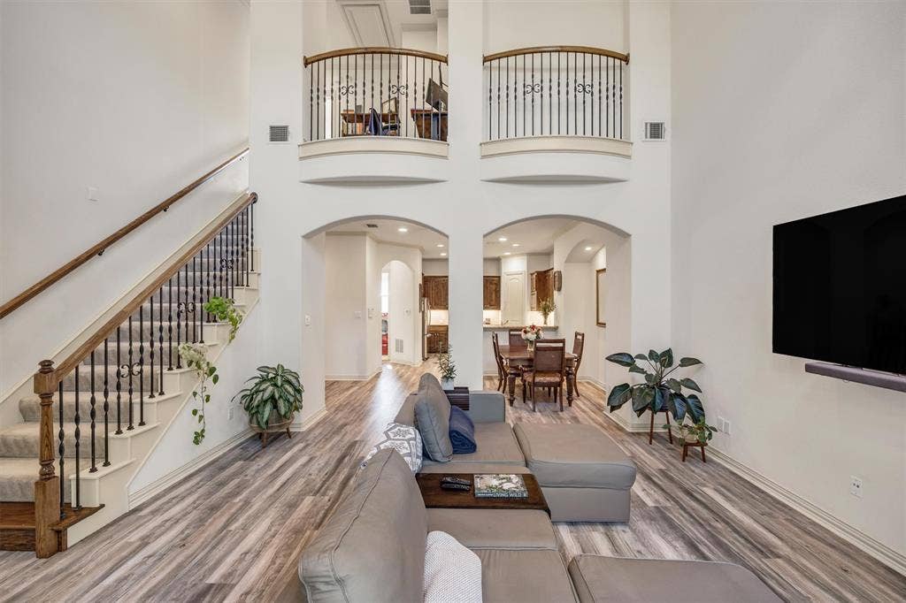 8249 Short Street, Frisco, TX 75034 Two-story living area featuring wood-finish flooring, a carpeted staircase with wood and iron banisters, and arched doorways