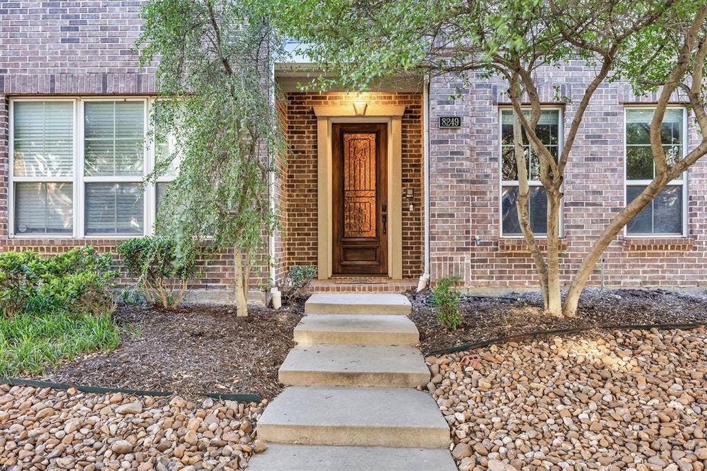 8249 Short Street, Frisco, TX 75034 Brick exterior with multiple windows, a wood-paneled front door, and a concrete pathway leading to the entrance