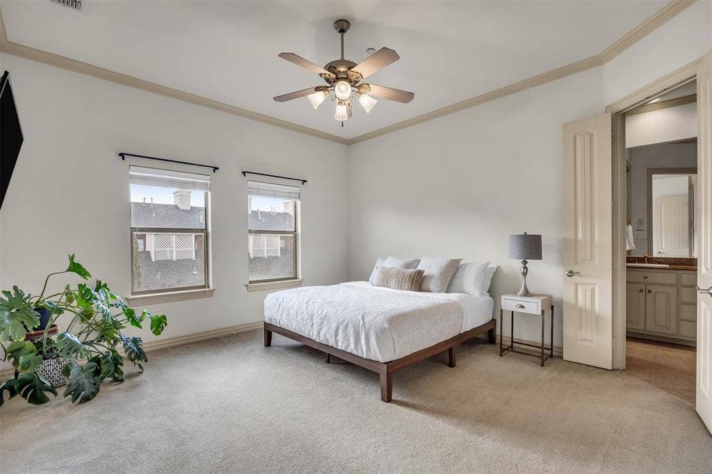 8249 Short Street, Frisco, TX 75034 Recessed ceiling with crown molding, ceiling fan with integrated lighting, two windows with roller shades, carpet flooring, and an open doorway to a bathroom with a vanity