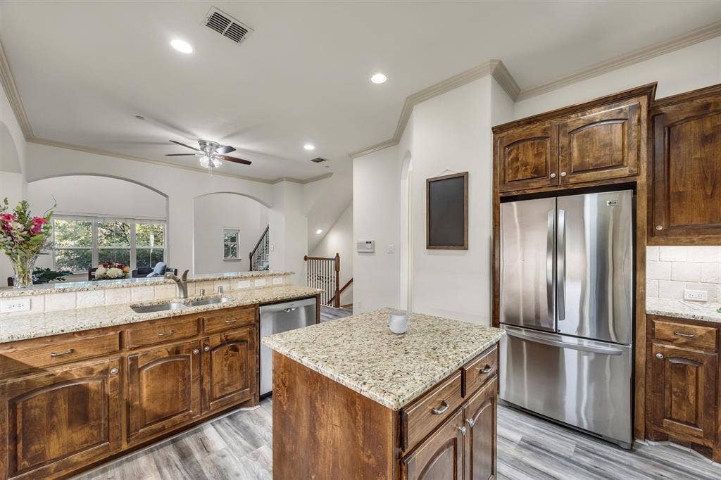 8249 Short Street, Frisco, TX 75034 Kitchen featuring wood-finish flooring, wood cabinetry, granite countertops, and stainless steel appliances