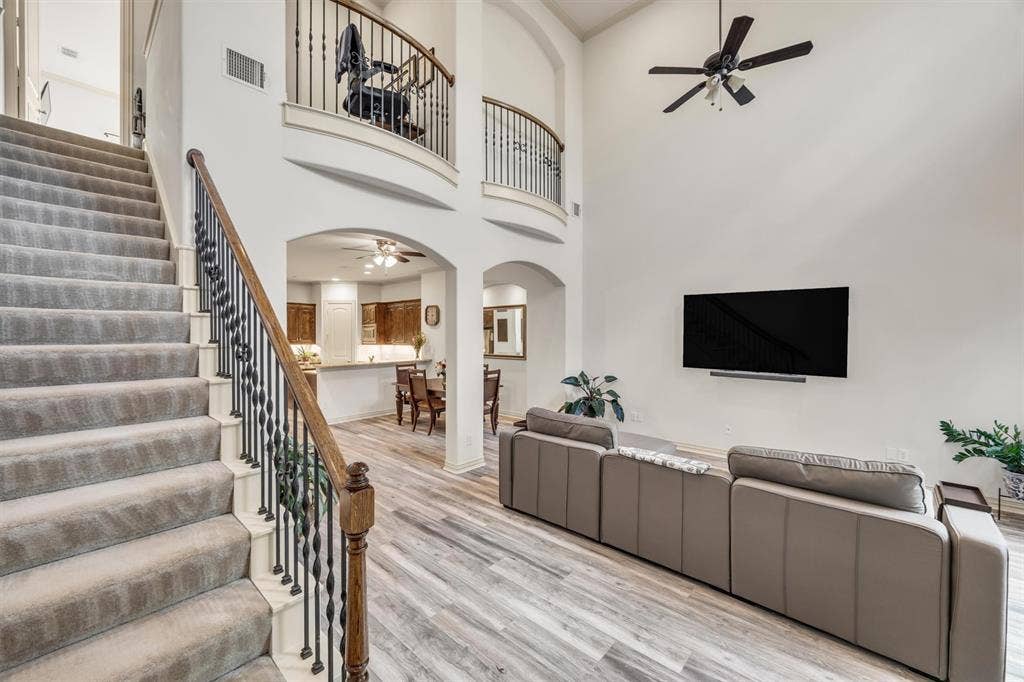 8249 Short Street, Frisco, TX 75034 Two-story living area with high ceilings, wood-finish flooring, and a carpeted staircase with an ornamental metal baluster