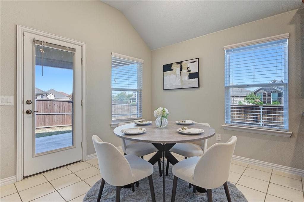 Vaulted ceiling, transom window, glass-panel door, tile flooring, and two windows with blinds