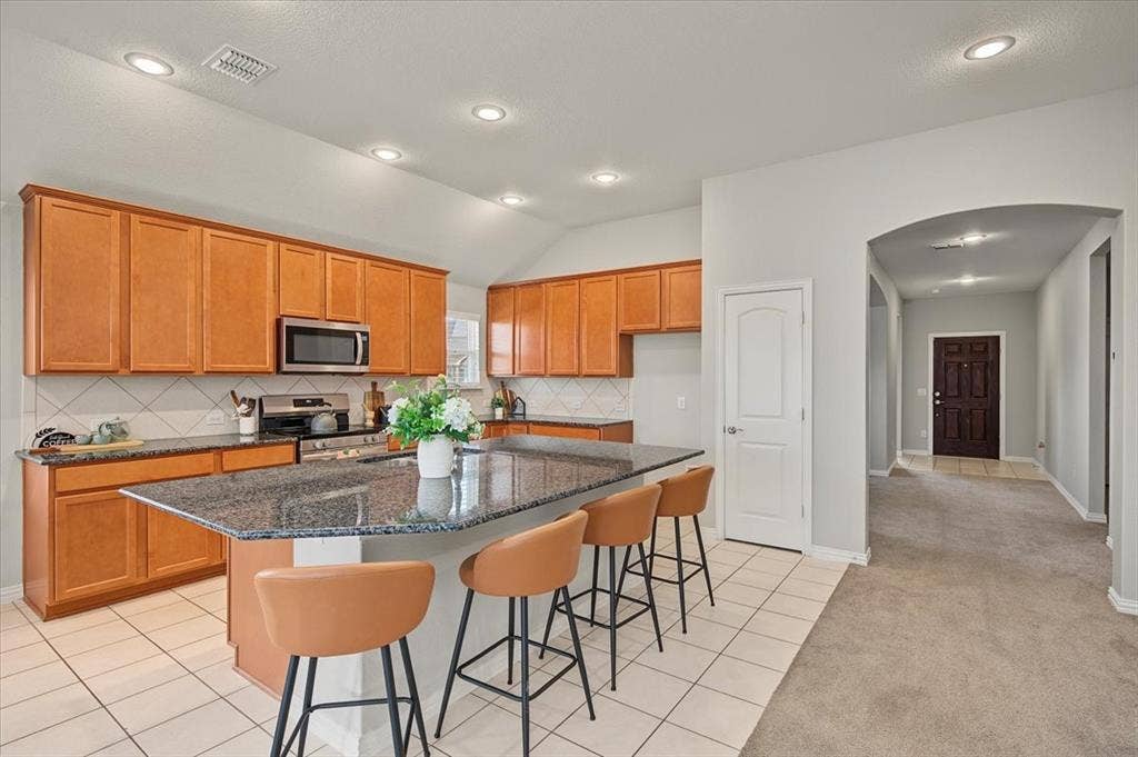 Kitchen featuring a center island with a stone countertop, wood cabinetry, tile backsplash, and stainless steel microwave