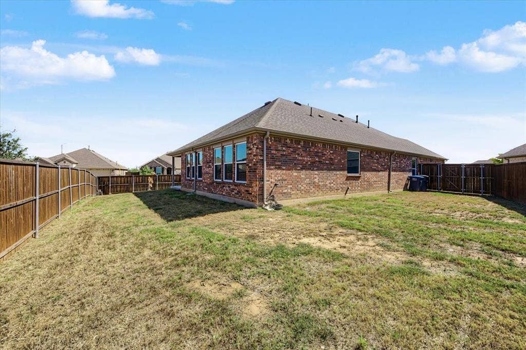 Brick exterior featuring a hip roof, multiple windows, and a wood privacy fence enclosing the yard