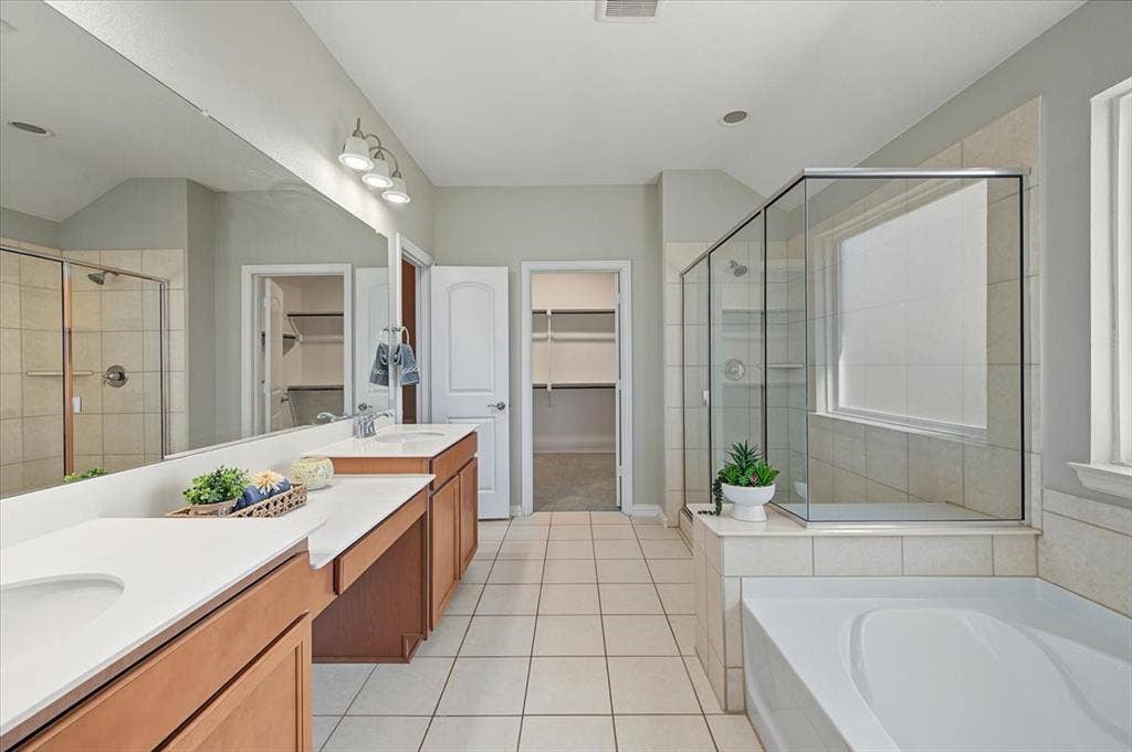 Dual vanities with undermount sinks, separate shower enclosure with glass surround, built-in soaking tub, and tile flooring