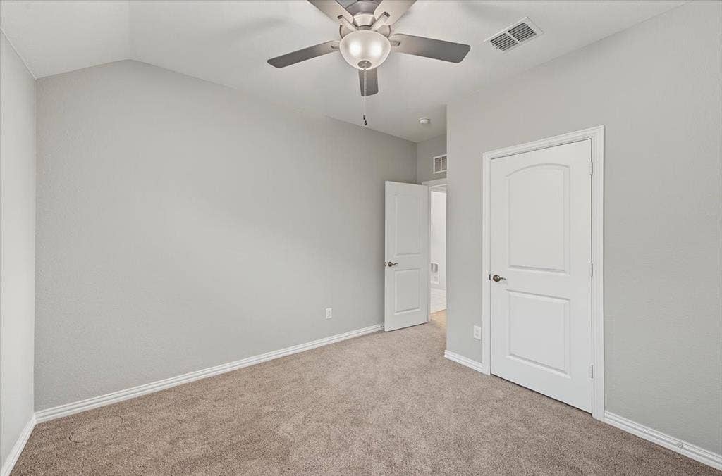 Vaulted ceiling with a flush-mount ceiling fan, neutral wall paint, and soft carpeting